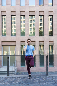 Full length of man standing on footpath against building in city