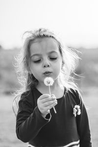 Girl blowing dandelion while standing on field