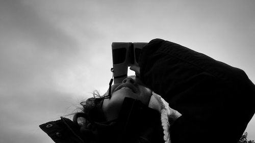 Low angle view of woman looking through binoculars against sky