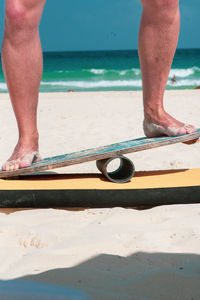 Low section of man balancing on surfboard at beach