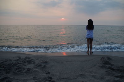 Rear view of woman standing on beach at sunset