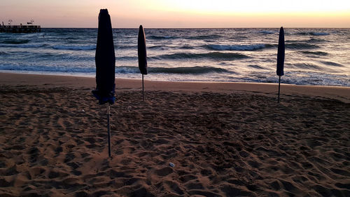 Wooden posts on beach against sky during sunset