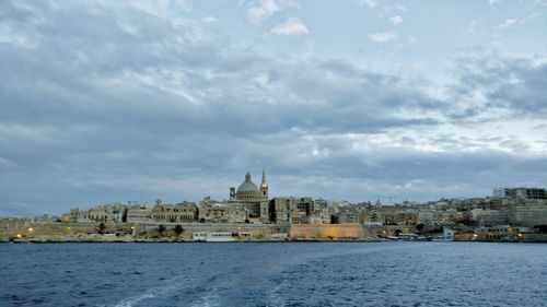 View of city at waterfront against cloudy sky