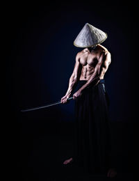 Shirtless muscular man holding sword against blue background