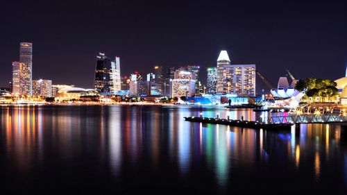 Illuminated buildings by river against clear sky at night