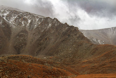 Rocky mountain range in the snow against the background of the sky with clouds, bad weather