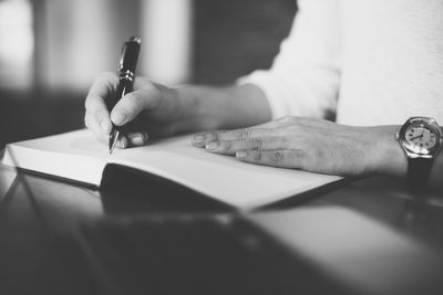 Midsection of woman writing in diary at table