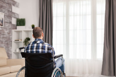 Rear view of handicapped sitting on wheelchair at home