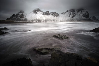 Scenic view of sea by snowcapped mountains against sky