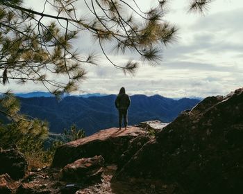 Rear view of woman standing on rock against sky