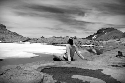 Rear view of man sitting on rock against sea