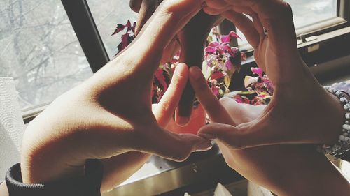 Cropped image of friends making peace logo by window at home