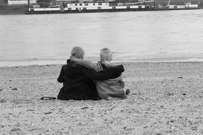 Rear view of siblings sitting with arms around at beach