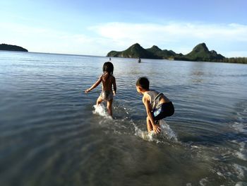 Siblings enjoying in sea against sky