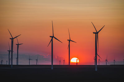 Silhouette wind turbines on field against orange sky