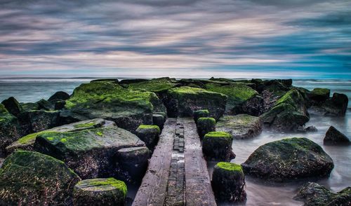 Pier and moss covered rocks by sea against sky