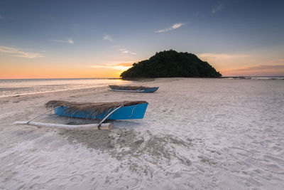 Boats at sandy beach against sky during sunset