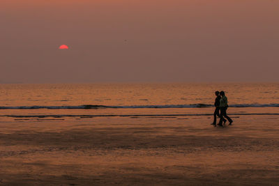 Silhouette people on beach against sky during sunset