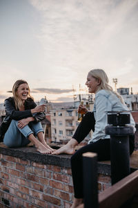 Young woman sitting outdoors against sky in city at sunset