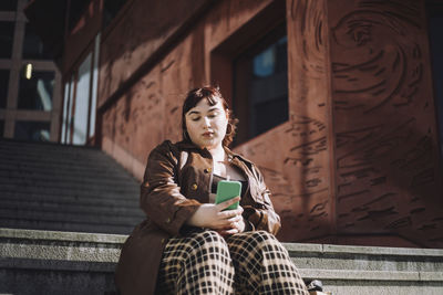 Young woman taking selfie through smart phone while sitting on steps