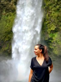 Woman looking away while standing against waterfall