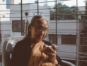 Senior woman looking at phone while sitting in balcony