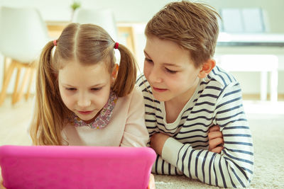 Siblings using digital tablet while lying at home