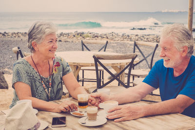 Smiling senior couple sitting at cafe against sea