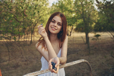 Portrait of smiling young woman holding plant against trees