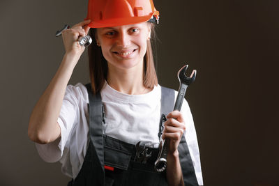 Portrait of young man holding hardhat while standing against black background