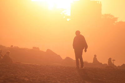 Silhouette people standing on land against sky during sunset