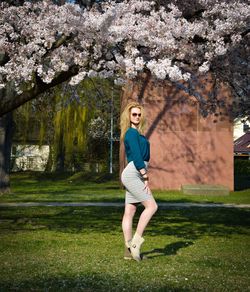 Full length portrait of woman standing on grass by cherry tree