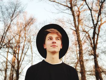 Low angle view of young man looking away while standing against sky in forest