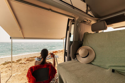 Rear view of woman sitting on chair at beach