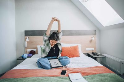 Young asian artist stretches on her bed, preparing for a productive day of digital art creation.