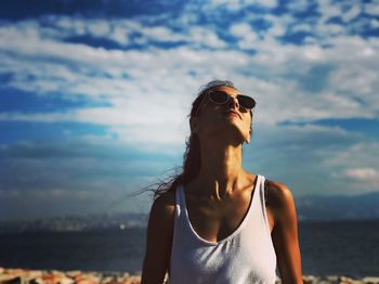 Young woman wearing sunglasses at beach against sky