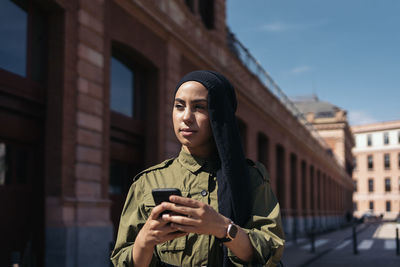 Portrait of young woman standing against building