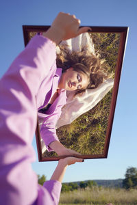 Portrait of woman holding plant against sky