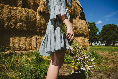 Young girl in rubber boots with flowers standing against the background of straw bales on country 