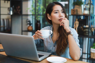 Young woman using phone while sitting at table