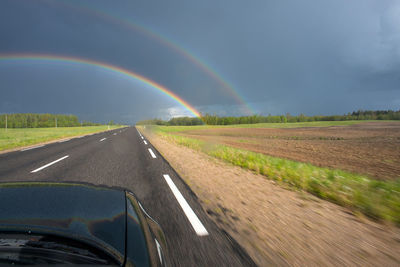 Rainbow over road amidst field against sky