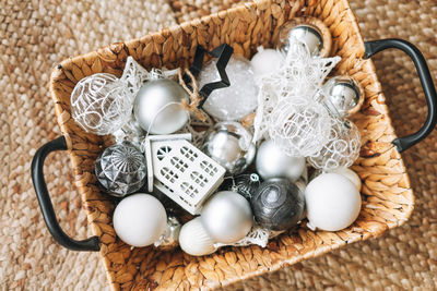 Wicker basket with white and silver christmas tree toys and balls on the floor, top view