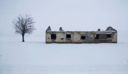 Abandoned building on snow covered field against sky