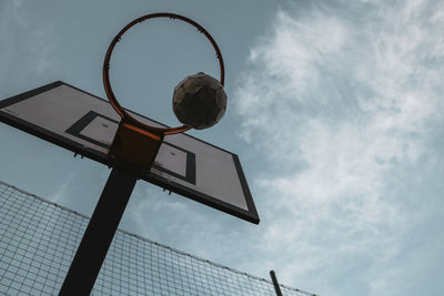 Low angle view of soccer ball over basketball hoop against sky