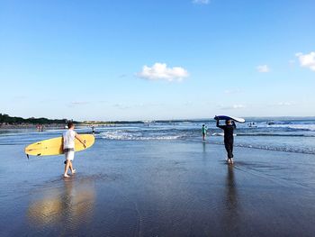 People with surfboards at beach against sky