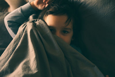 A little boy hides under the covers in bed and smiles.