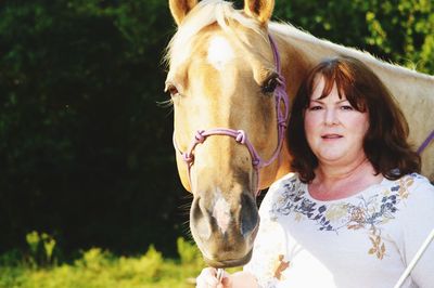 Portrait of senior woman with horse standing in forest