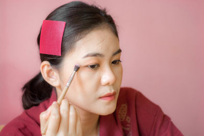 Close-up of young woman applying make-up against pink background