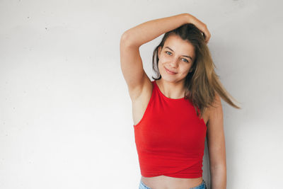 Portrait of smiling young woman standing against white wall