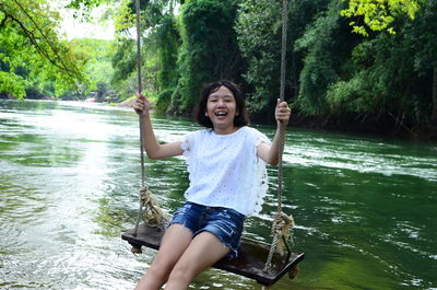 Happy boy sitting on tree by water